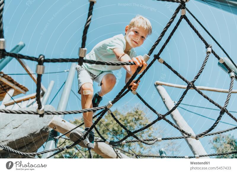 Junge klettert bei Sonnenschein auf Spinnennetz im öffentlichen Park Farbaufnahme Farbe Farbfoto Farbphoto Außenaufnahme außen draußen im Freien Tag