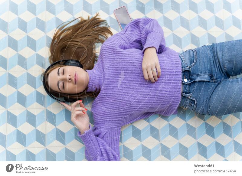 Porträt einer jungen Frau mit geschlossenen Augen, die auf dem Boden liegt und mit Kopfhörern Musik hört Leute Menschen People Person Personen Europäisch