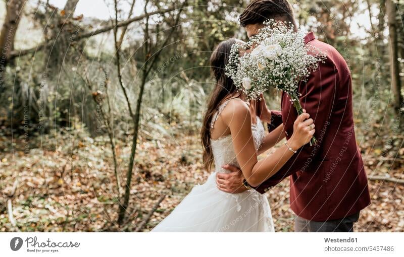 Unerkennbare Braut und Bräutigam küssen sich im Wald hinter einem Blumenstrauss Hochzeit heiraten Heirat Hochzeiten Küsse Kuss Bräute Blumenstrauß Bouquet