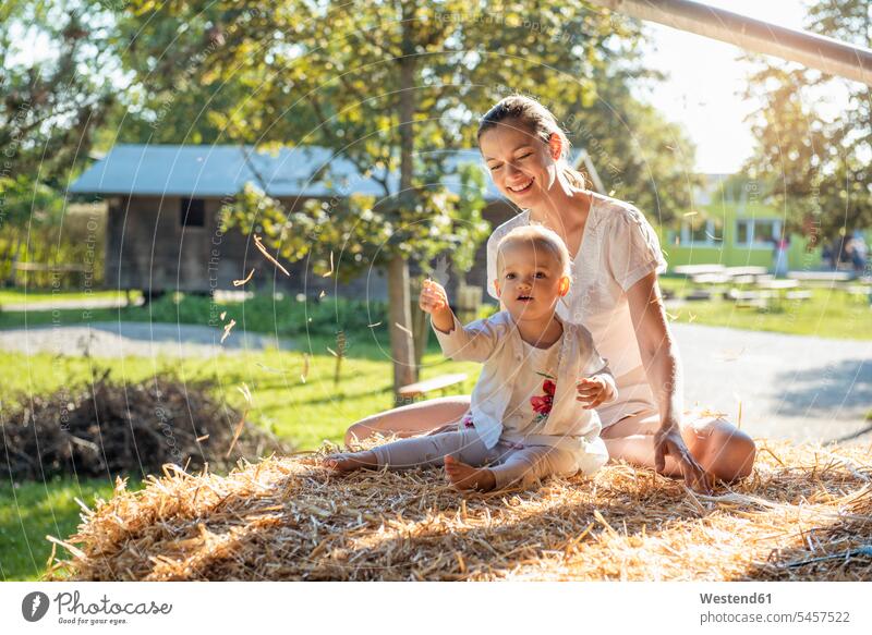 Glückliche Mutter und kleine Tochter spielen mit Stroh auf einem Bauernhof Mamas Mami Mutti Mütter Muetter Mamis Muttis Farmen Bauernhoefe Bauernhöfe Töchter