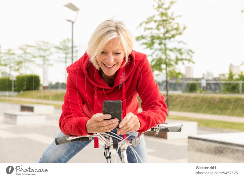 Lächelnde ältere Frau mit Stadtfahrrad beim Telefonieren Fahrrad Bikes Fahrräder Räder Rad lächeln Zuversicht Zuversichtlich Selbstvertrauen selbstbewusst