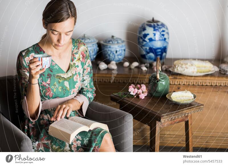Junge Frau trinkt eine Tasse Tee, während sie zu Hause ein Buch liest Bücher weiblich Frauen Tees lesen Lektüre trinken Erwachsener erwachsen Mensch Menschen