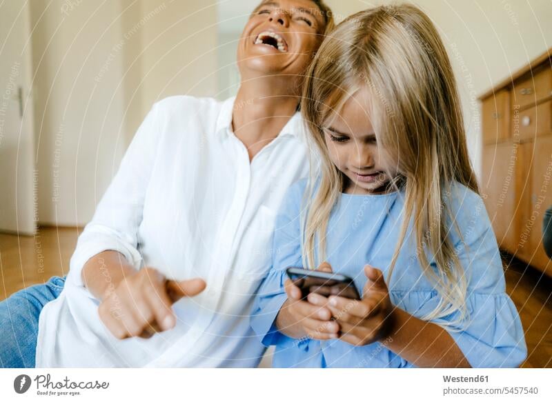 Lachende Mutter und Tochter schauen auf Smartphone Töchter ansehen iPhone Smartphones lachen Mami Mutti Mütter Mama Zuhause zu Hause daheim Kind Kinder Familie