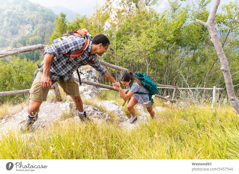 Italien, Massa, Mann hilft einer jungen Frau beim Besteigen einer Stufe beim Wandern in den Alpi Apuane Bergen helfen mithelfen Hilfsbereitschaft beistehen