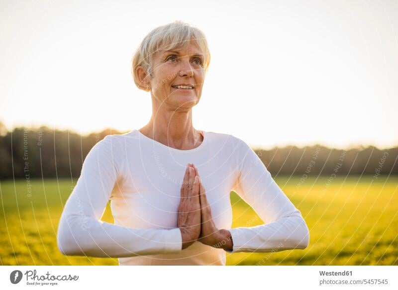 Senior Frau macht Yoga auf ländlichen Wiese bei Sonnenuntergang Seniorin älter Seniorinnen alt auf dem Land auf dem Lande Wiesen Yoga-Übungen Yogauebungen