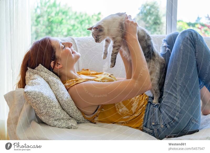 Junge Frau liegt zu Hause auf der Couch und hält ihre Katze Leute Menschen People Person Personen Alleinstehende Alleinstehender Singles Unverheiratete