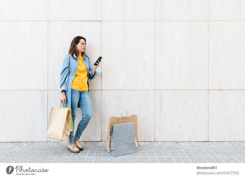 Junge brünette Frau benutzt Smartphone nach dem Einkauf Leute Menschen People Person Personen Europäisch Kaukasier kaukasisch 1 ein Mensch eine nur eine Person