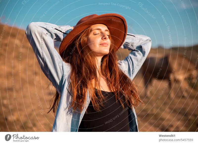 Junge Frau mit Hut entspannt und genießt die ländliche Landschaft weiblich Frauen genießen geniessen Genuss entspanntheit relaxt Landschaften Hüte Erwachsener
