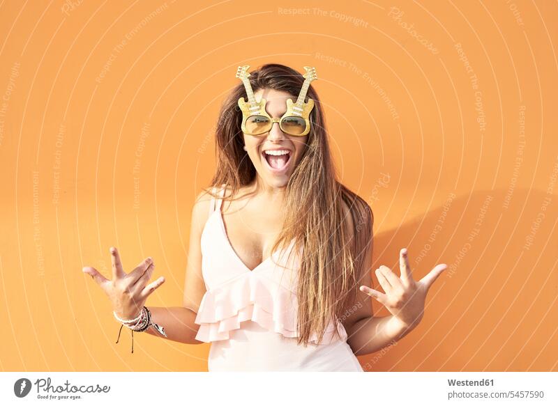 Porträt einer lächelnden jungen Frau mit Gitarren-Sonnenbrille vor orangem Hintergrund weiblich Frauen schreien rufen rufend Schrei schreiend Portrait Porträts