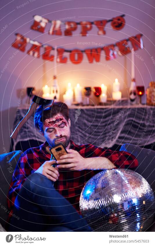 Gelangweilter Mann benutzt Handy auf Halloween-Party Smartphone iPhone Smartphones warten maskiert feiern Verabredung verabreden Parties Partys