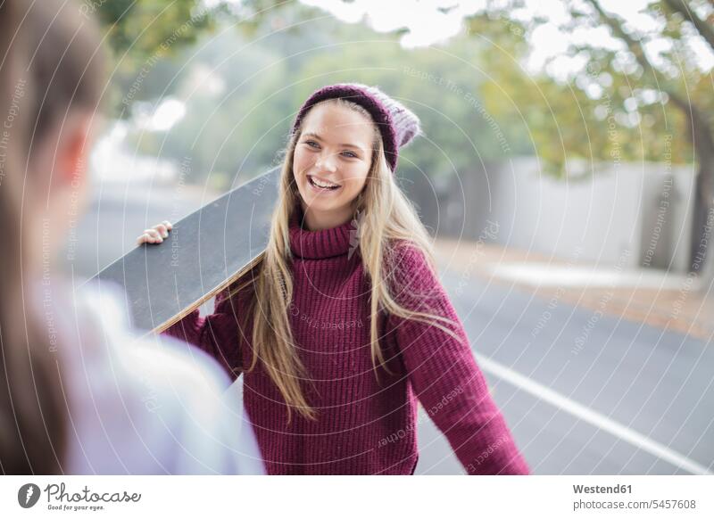 Lächelndes Teenager-Mädchen hält Skateboard-Treffen mit Freundin Freunde Rollbretter Skateboards lächeln Begegnung Teenagerin junges Mädchen Teenagerinnen