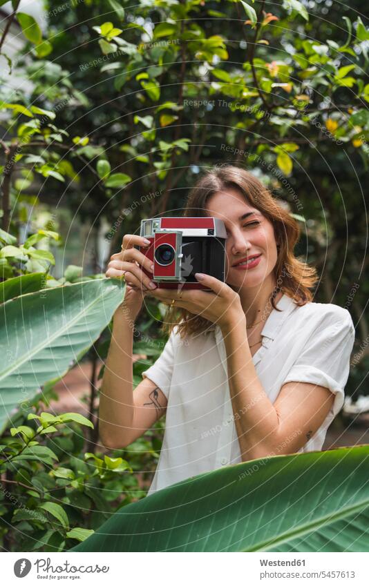 Junge Frau im Gewächshaus, die mit einer Sofortbildkamera fotografiert junge Frau junge Frauen fotografieren Polaroid-Kamera weiblich Erwachsener erwachsen