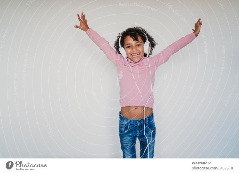 Porträt eines fröhlichen kleinen Mädchens mit rosa Rollkragenpullover, das mit Kopfhörern Musik hört Leute Menschen People Person Personen 1 Ein ein Mensch