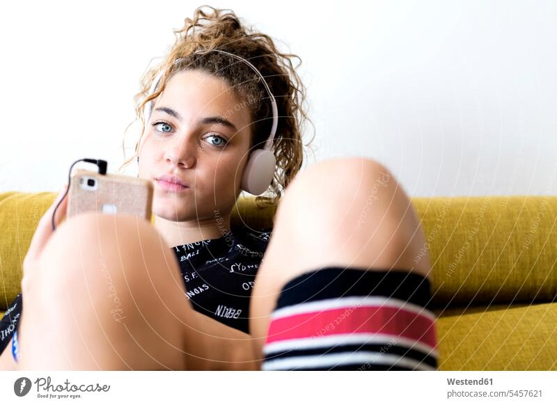 Porträt des Mädchens sitzt auf der Couch hören Musik mit Kopfhörern und Smartphone Sofa Couches Liege Sofas iPhone Smartphones weiblich sitzen sitzend hoeren