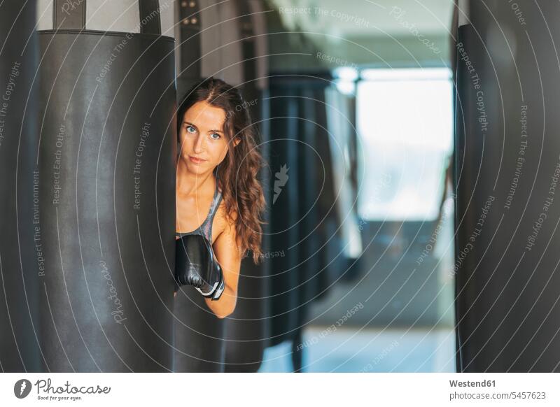 Porträt einer Frau mit Boxhandschuhen hinter einem Sandsack in einer Turnhalle stehend steht fit gesund Gesundheit Muße Kampfkunst Kampfsportart Kampfsportarten