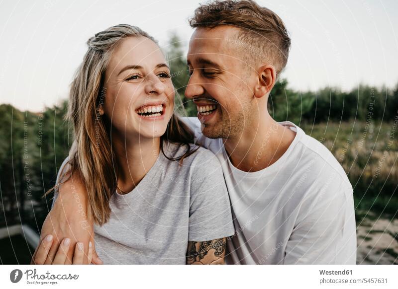 Porträt eines jungen lachenden Paares T-Shirts Arm umlegen Umarmung Umarmungen abends freuen Frohsinn Fröhlichkeit Heiterkeit Glück glücklich sein glücklichsein