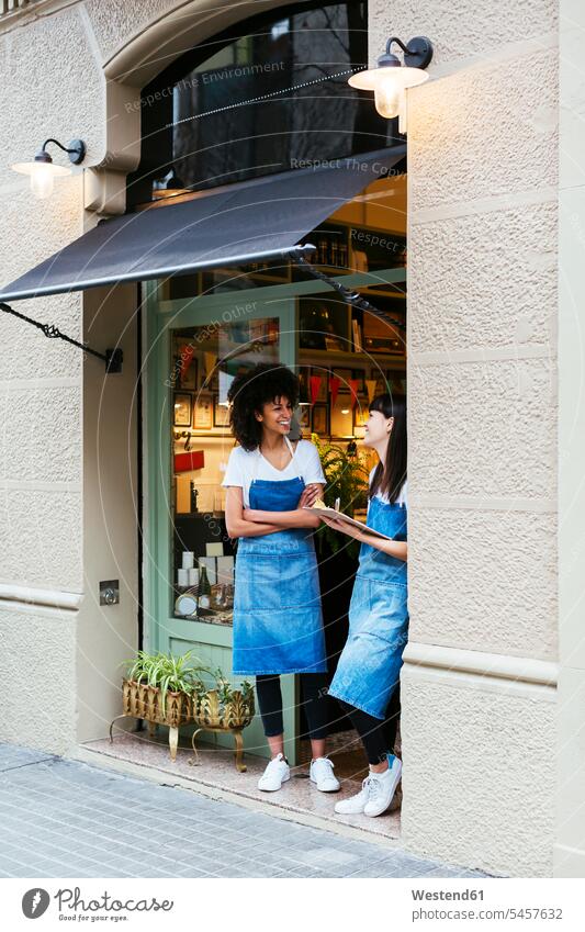 Zwei glückliche Frauen stehen in der Eingangstür eines Geschäfts Eingangstuer Eingangstüren Eingangstueren stehend steht weiblich Shop Laden Läden Geschäfte