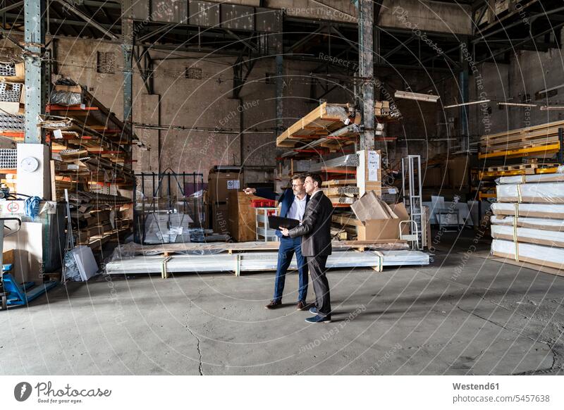 Zwei Geschäftsleute mit Ordner im Gespräch in einem alten Lagerhaus altes alter sprechen reden Lagerhalle Lagerhallen Mappe Mappen Depot Deutschland