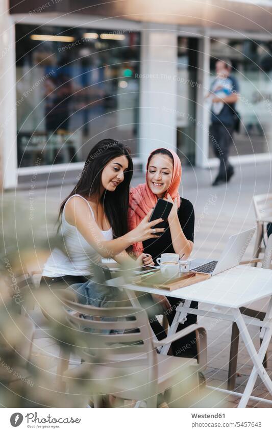 Zwei Freunde sitzen zusammen auf einem Bürgersteig Cafe mit Handy Selbstportrait Selfies sich selbst fotografieren Tisch Tische Laptop benutzen Laptop benützen