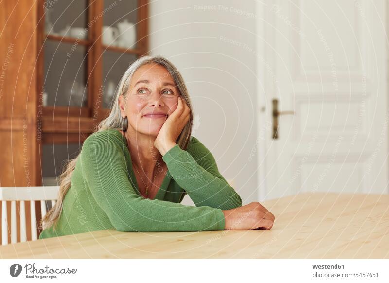 Lächelnde Frau träumt, während sie zu Hause am Tisch sitzt Deutschland Innenaufnahme Innenaufnahmen innen drinnen Tag Tageslichtaufnahme Tageslichtaufnahmen
