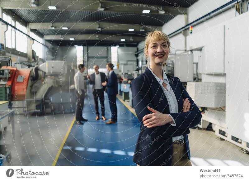 Porträt einer selbstbewussten Geschäftsfrau in einer Fabrik mit Kollegen im Hintergrund Arbeitskollege Arbeitskollegen Job Berufe Berufstätigkeit Beschäftigung