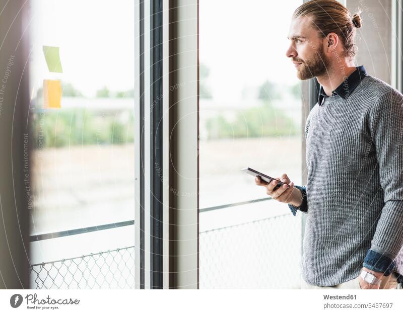 Junger Geschäftsmann mit Mobiltelefon schaut aus dem Fenster Handy Handies Handys Mobiltelefone Zuversicht Zuversichtlich Selbstvertrauen selbstbewusst