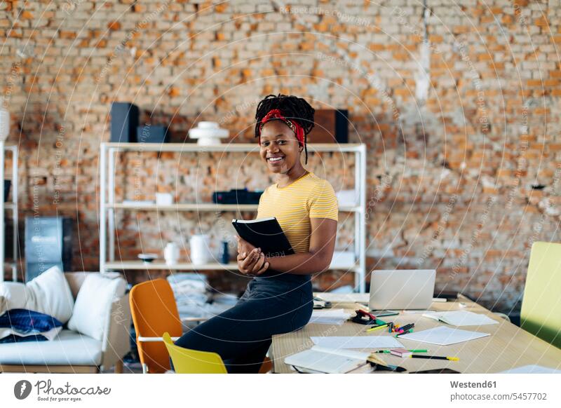 Porträt einer selbstbewussten jungen Frau am Tisch im Büro mit einem Notizbuch in der Hand Schwarze Schwarzer eine Person junge Frau 20-25 Jahre Praktikant