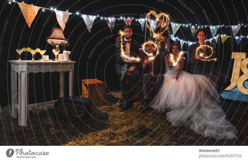 Hochzeitspaar und Freunde machen das Wort "Liebe" mit Wunderkerzen auf einer nächtlichen Party im Freien heiraten Heirat Hochzeiten glücklich Glück