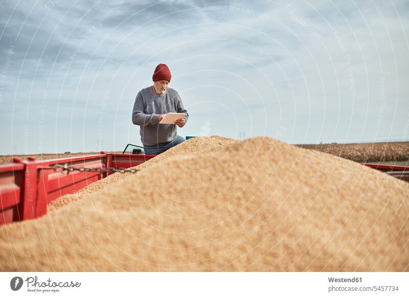 Landwirt verwendet digitales Tablett, während er am Traktor vor klarem Himmel steht Farbaufnahme Farbe Farbfoto Farbphoto Außenaufnahme außen draußen im Freien