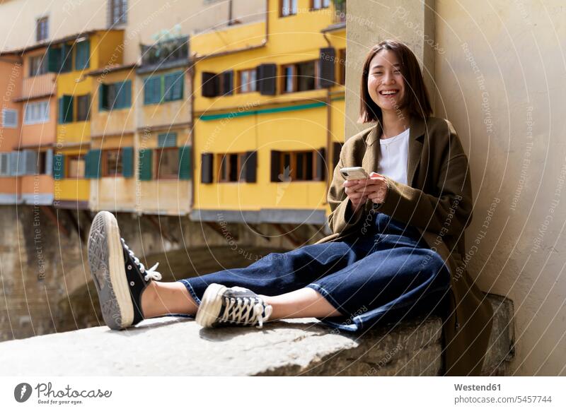 Italien, Florenz, glückliche junge Frau, die sich auf einer Mauer in der Stadt ausruht Wohnhaus Wohnhäuser Wohnhaeuser wohnen fröhlich Fröhlichkeit Frohsinn