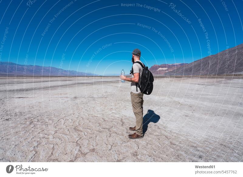USA, Kalifornien, Death Valley, Mann mit Rucksack und Wasserflasche steht in der Wüste und schaut in die Ferne Rucksäcke Wüsten Männer männlich Flasche Flaschen