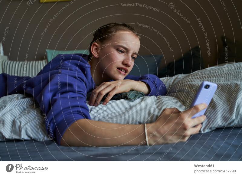 Porträt eines Mädchens, das zu Hause auf dem Bett liegt und ein Smartphone für einen Video-Chat benutzt Betten Telekommunikation Handies Handys Mobiltelefon