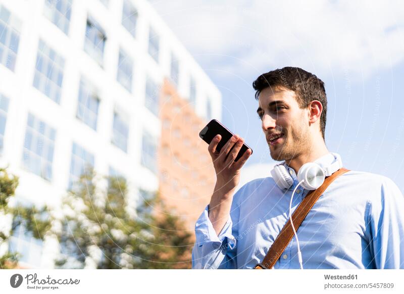 Junger Mann benutzt Smartphone, Kopfhörer um den Hals in der Stadt Hemden Kopfhoerer Telekommunikation telefonieren Handies Handys Mobiltelefon Mobiltelefone