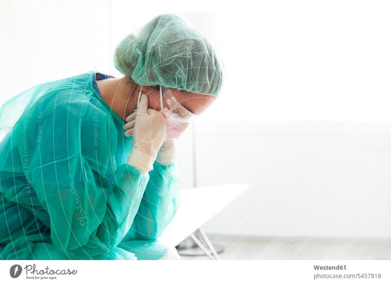 Trauriger Arzt in Arbeitsschutzkleidung sitzt im Krankenhaus am Fenster Farbaufnahme Farbe Farbfoto Farbphoto Innenaufnahme Innenaufnahmen innen drinnen Medizin