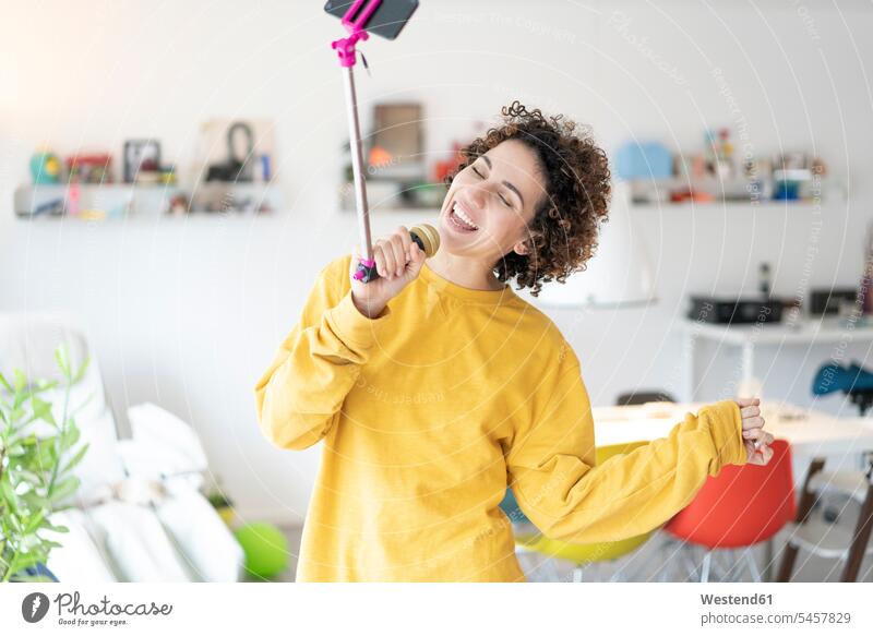 Sorglose Frau singt zu Hause in ein Mikrofon, das an einem Selfie-Stick befestigt ist Unbeschwert singen Musik Zuhause daheim Mikrophone Mikrofone weiblich