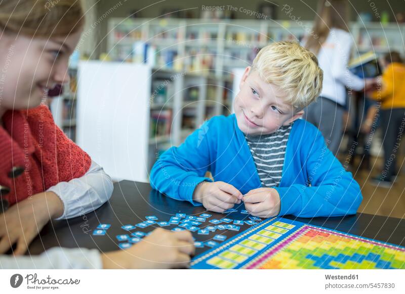 Schülerinnen und Schüler bei einem Brettspiel in der Schulbibliothek lächeln sich an ansehen Brettspiele Schule Schulen Bücherei spielen Schulkind Schueler