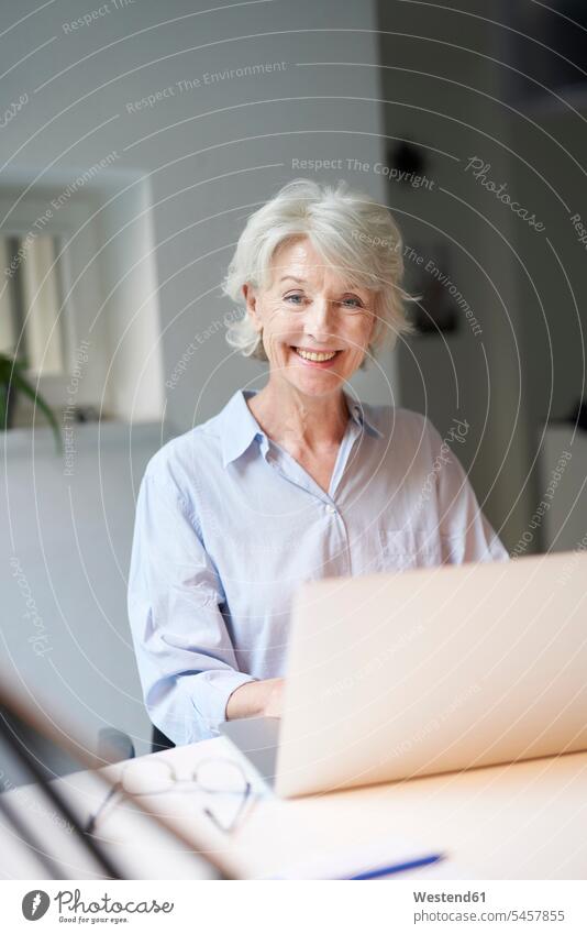 Porträt einer lächelnden reifen Frau mit Laptop am Schreibtisch Job Berufe Berufstätigkeit Beschäftigung Jobs Businesskleidung Tische Arbeitstisch Schreibtische