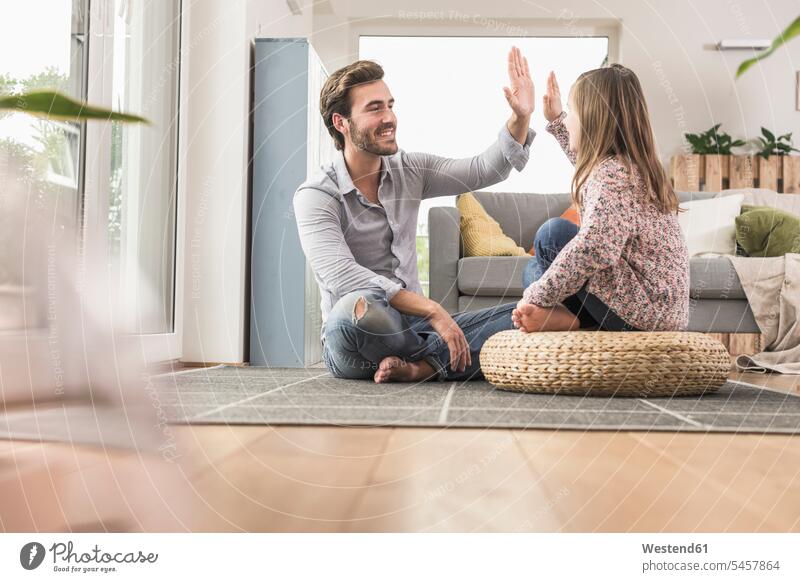 Junger Mann und kleines Mädchen sitzen zu Hause, geben High Five optimistisch Optimismus auf dem Boden sitzen auf dem Boden sitzend Ganzkörperansicht