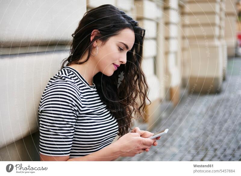 Junge Frau benutzt Handy in der Stadt staedtisch städtisch Mobiltelefon Handies Handys Mobiltelefone weiblich Frauen Außenaufnahme draußen im Freien Telefon