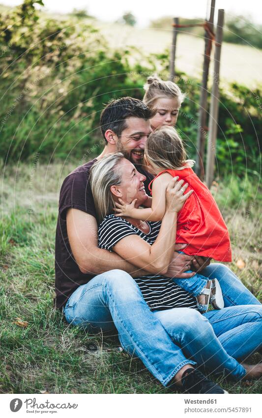 Glückliche Familie mit zwei Töchtern sitzt auf einer Wiese Familien spielen Tochter lächeln glücklich glücklich sein glücklichsein Natur Mensch Menschen Leute
