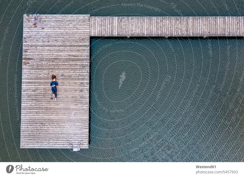 Luftaufnahme einer jungen Triathletin, die auf einem Steg an einem See liegt Leute Menschen People Person Personen Europäisch Kaukasier kaukasisch 1 Ein