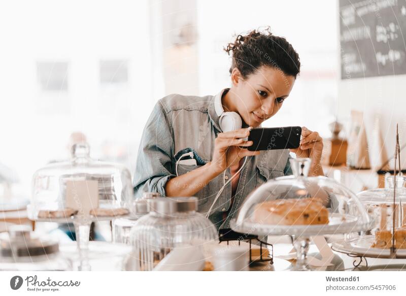 Frau fotografiert Kuchen im Café mit ihrem Smartphone Cafe Kaffeehaus Bistro Cafes Cafés Kaffeehäuser Kopfhörer Kopfhoerer iPhone Smartphones weiblich Frauen