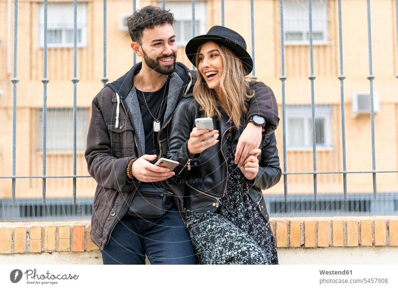 Porträt eines lachenden jungen Paares mit ihren Mobiltelefonen in der Stadt Leute Menschen People Person Personen Europäisch Kaukasier kaukasisch 2 2 Menschen