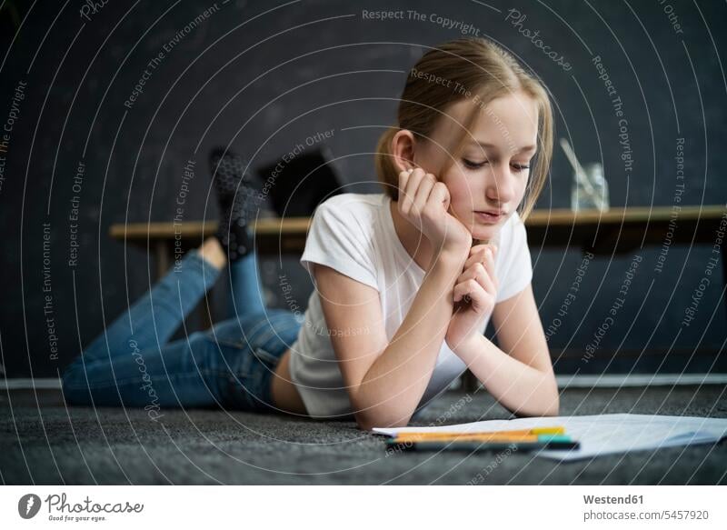 Mädchen liegt auf Teppich und lernt zu Hause Stifte Teppiche Lektüre schwarze schwarzen schwarzer schwarzes daheim Ausbildung Boeden Böden drinnen