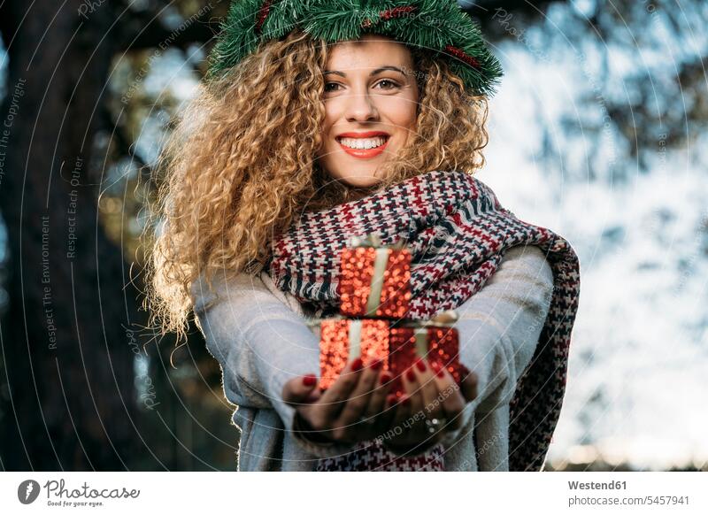 Porträt einer lächelnden jungen Frau mit Weihnachtskranz auf dem Kopf, die ein Weihnachtsgeschenk überreicht Schals überreichen abends freuen Frohsinn