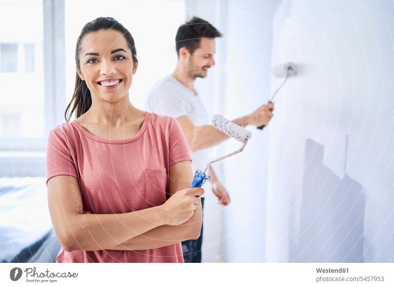 Porträt einer glücklichen Frau, die eine Wand mit ihrem Freund in einer neuen Wohnung bemalt Glück glücklich sein glücklichsein Wände Waende wohnen Wohnungen