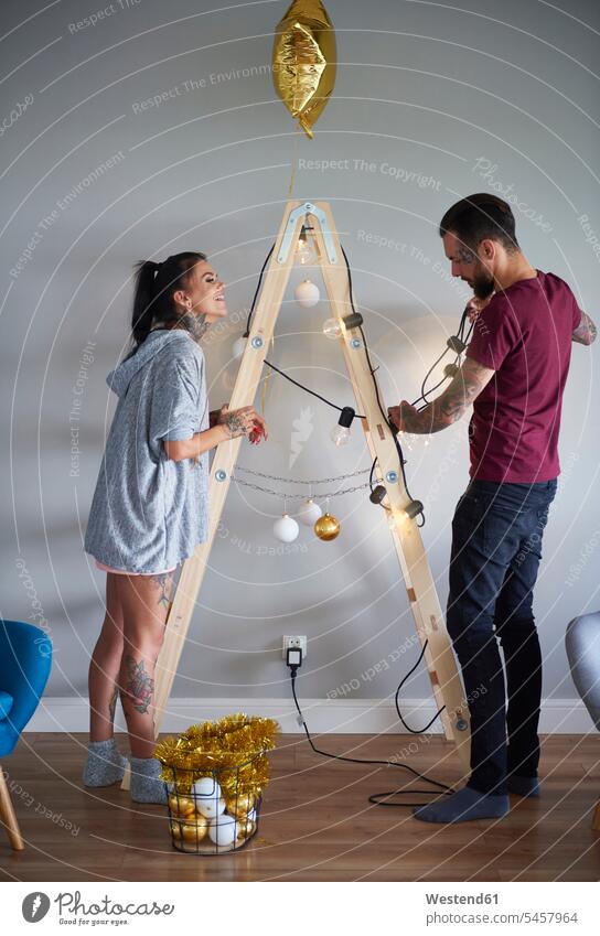 Modernes Paar dekorieren das Haus zur Weihnachtszeit mit Leiter als Weihnachtsbaum Weihnachten Christmas X-Mas X mas Zuhause zu Hause daheim Pärchen Paare