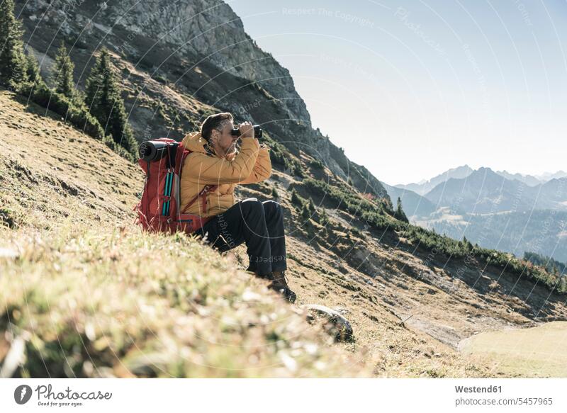 Österreich, Tirol, Mann macht Pause beim Wandern in den Bergen und schaut durch ein Fernglas Wandertour Gebirge Berglandschaft Gebirgslandschaft Gebirgskette