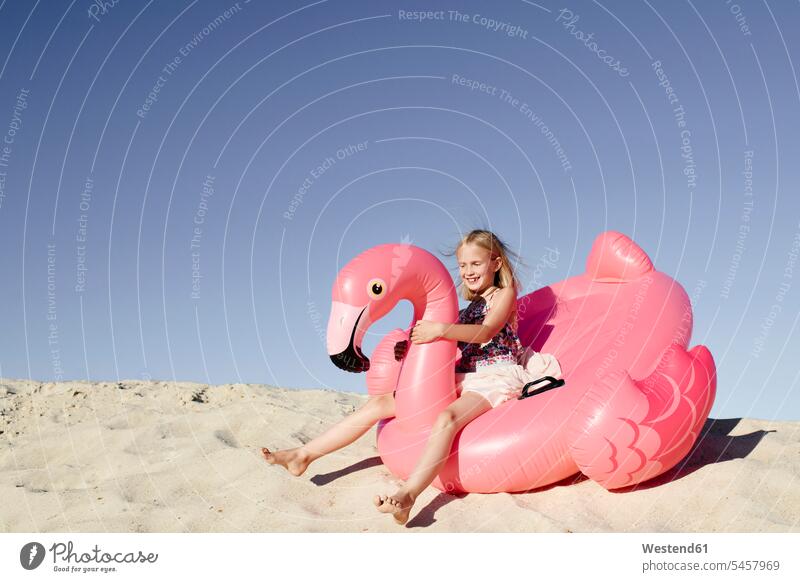 Lächelndes kleines Mädchen mit Flamingo-Pool schwimmt auf dem Sand Luftmatratzen sitzend sitzt Jahreszeiten sommerlich Sommerzeit pinkfarben rosa Muße Spass