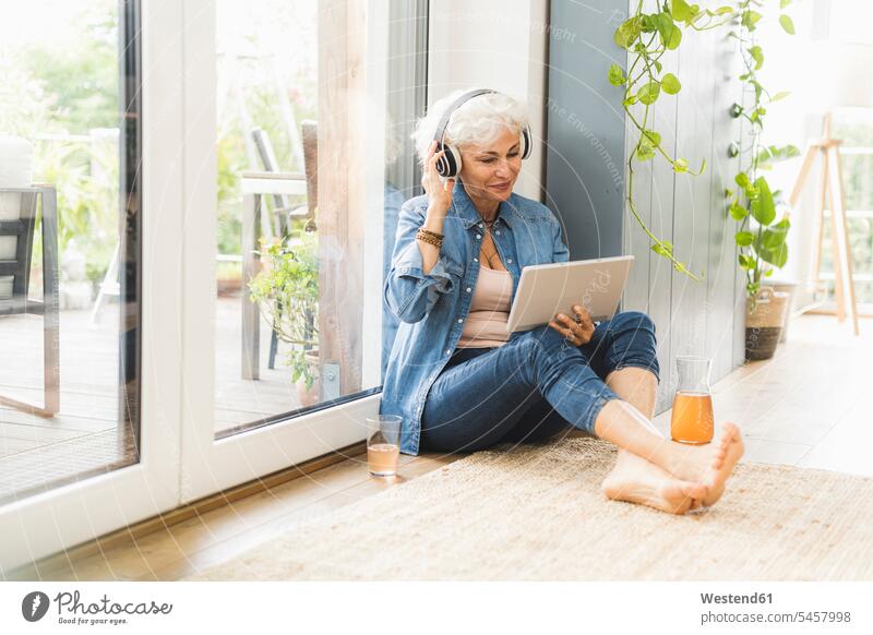 Reife Frau hört Musik, während sie an einem digitalen Tablet arbeitet Farbaufnahme Farbe Farbfoto Farbphoto Innenaufnahme Innenaufnahmen innen drinnen Tag